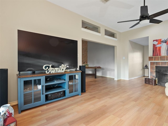 living room with a tiled fireplace, ceiling fan, and light wood-type flooring