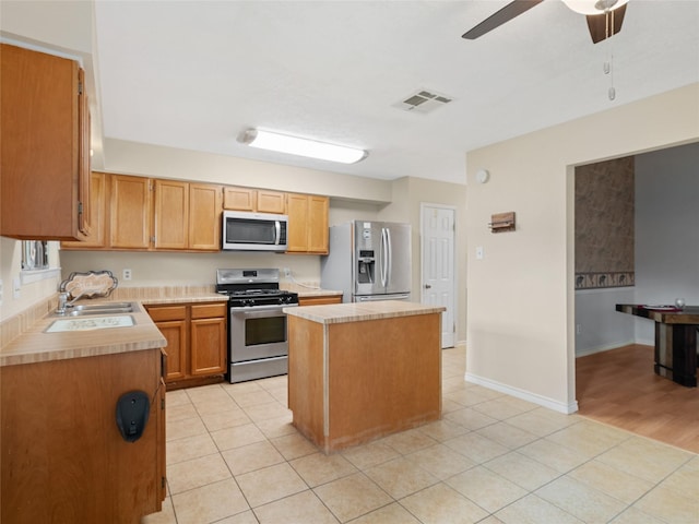 kitchen featuring sink, light tile patterned floors, ceiling fan, stainless steel appliances, and a center island