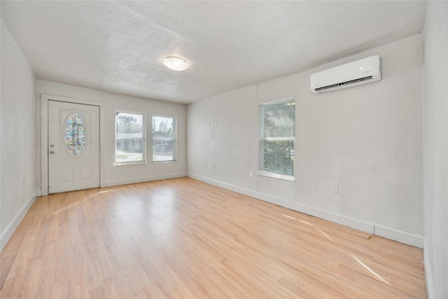 empty room with a wall mounted air conditioner, light hardwood / wood-style floors, a textured ceiling, and plenty of natural light