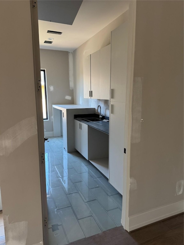 kitchen featuring baseboards, white cabinets, light countertops, a kitchen bar, and a sink