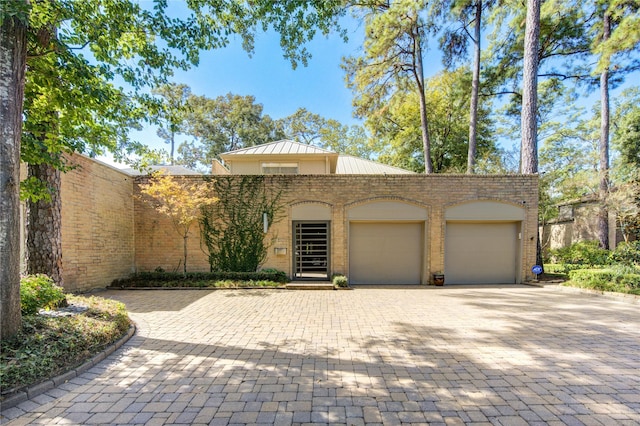 view of front facade featuring brick siding, metal roof, decorative driveway, an attached garage, and a standing seam roof