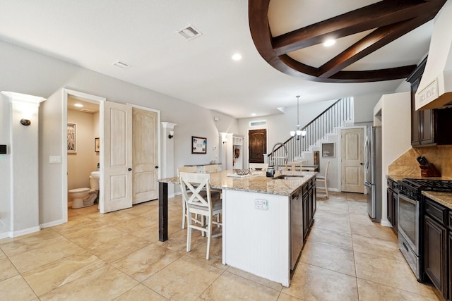 kitchen featuring dark brown cabinetry, light stone counters, appliances with stainless steel finishes, an island with sink, and custom range hood