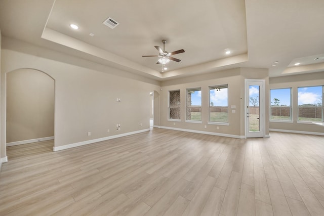 unfurnished living room with ceiling fan, a tray ceiling, and light wood-type flooring