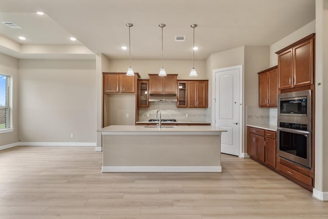 kitchen with tasteful backsplash, decorative light fixtures, an island with sink, and appliances with stainless steel finishes