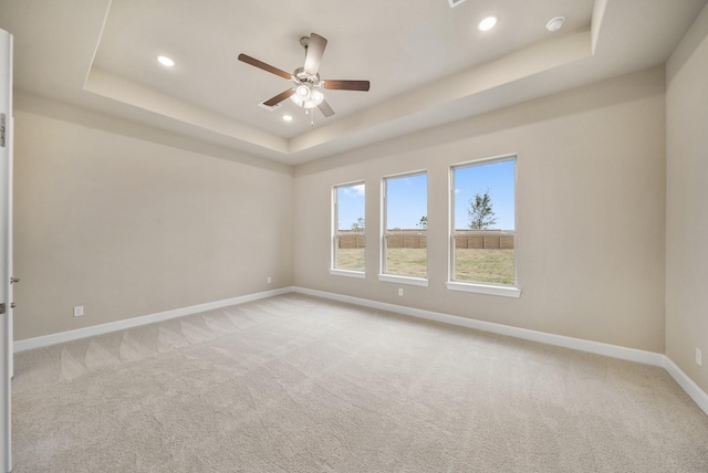 spare room with ceiling fan, a raised ceiling, and light carpet