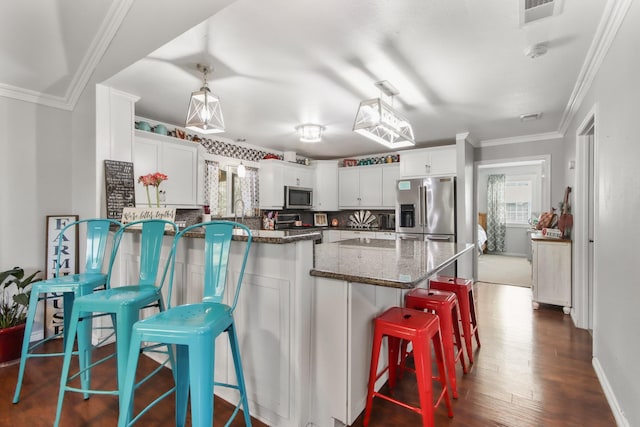 kitchen with white cabinetry, a breakfast bar area, stainless steel appliances, and dark stone counters