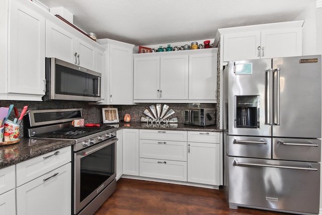 kitchen featuring backsplash, stainless steel appliances, dark stone counters, and white cabinets