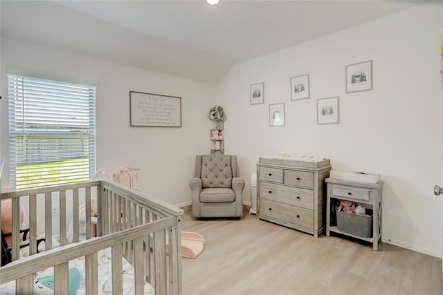 bedroom with a crib, vaulted ceiling, and light hardwood / wood-style flooring