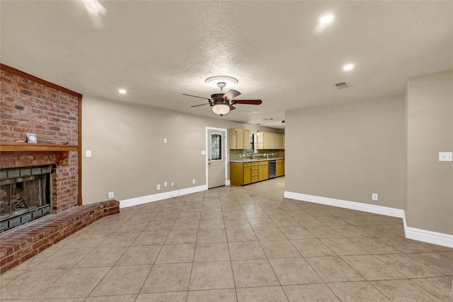 unfurnished living room featuring light tile patterned flooring, sink, ceiling fan, a brick fireplace, and a textured ceiling