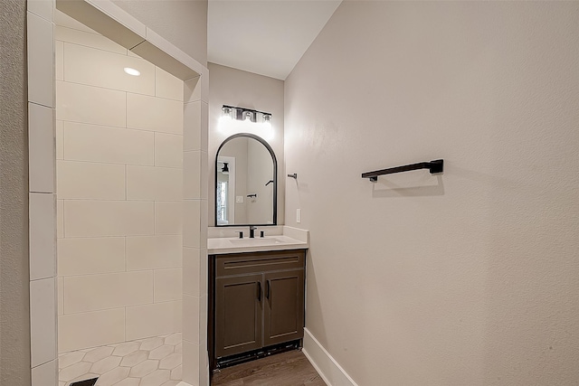 bathroom featuring hardwood / wood-style flooring, tiled shower, and vanity