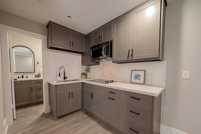 kitchen with black electric stovetop, light hardwood / wood-style floors, sink, and decorative backsplash