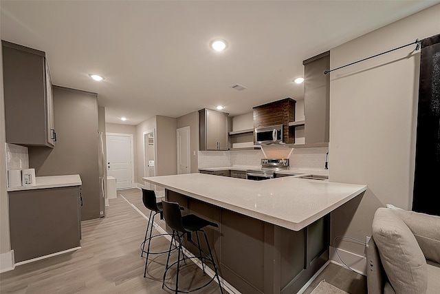 kitchen with a breakfast bar, gray cabinetry, light hardwood / wood-style flooring, kitchen peninsula, and stainless steel appliances