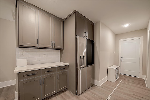 kitchen featuring gray cabinetry, decorative backsplash, light wood-type flooring, and stainless steel refrigerator with ice dispenser