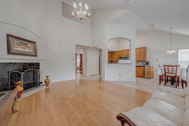 living room with high vaulted ceiling, a high end fireplace, a chandelier, and light hardwood / wood-style floors