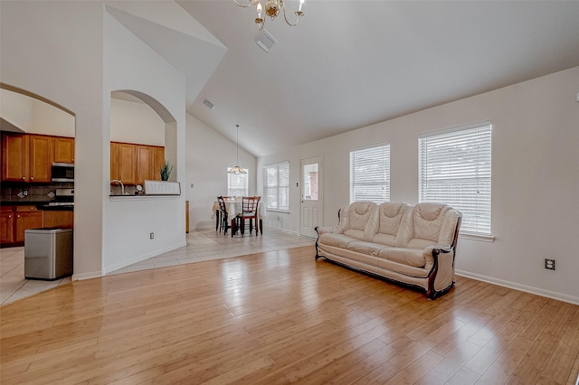 living room with an inviting chandelier, high vaulted ceiling, and light wood-type flooring