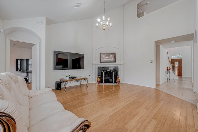 living room with a notable chandelier, a premium fireplace, light hardwood / wood-style flooring, and a high ceiling