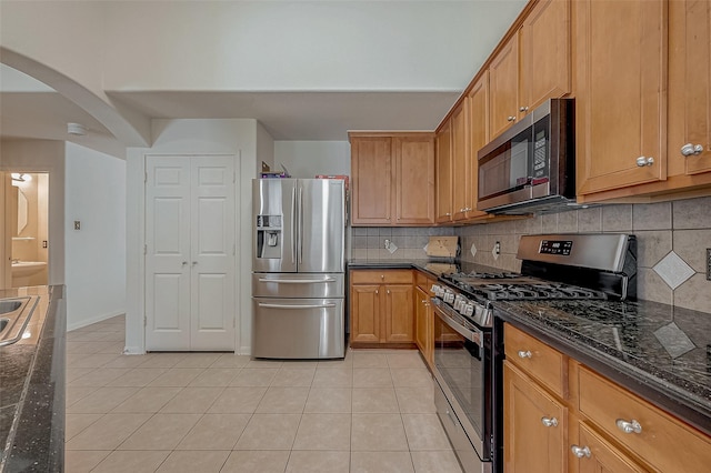 kitchen with light tile patterned flooring, appliances with stainless steel finishes, tasteful backsplash, and dark stone countertops