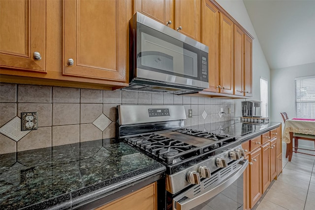 kitchen featuring appliances with stainless steel finishes, vaulted ceiling, decorative backsplash, and light tile patterned floors