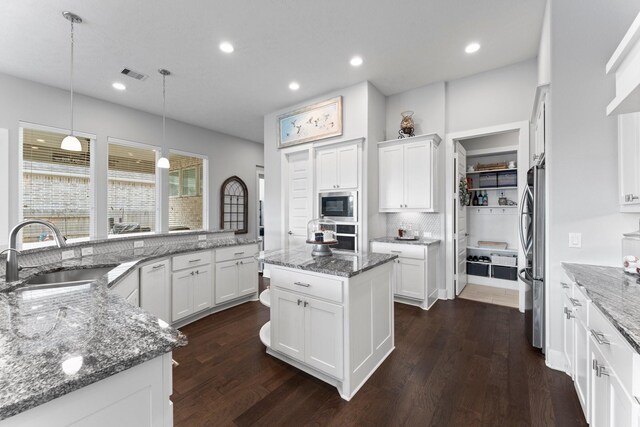 kitchen with sink, decorative light fixtures, appliances with stainless steel finishes, a kitchen island, and white cabinets