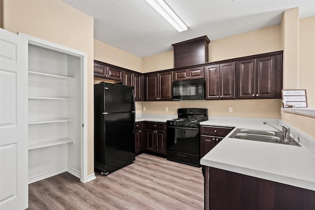 kitchen with dark brown cabinetry, sink, a textured ceiling, light wood-type flooring, and black appliances