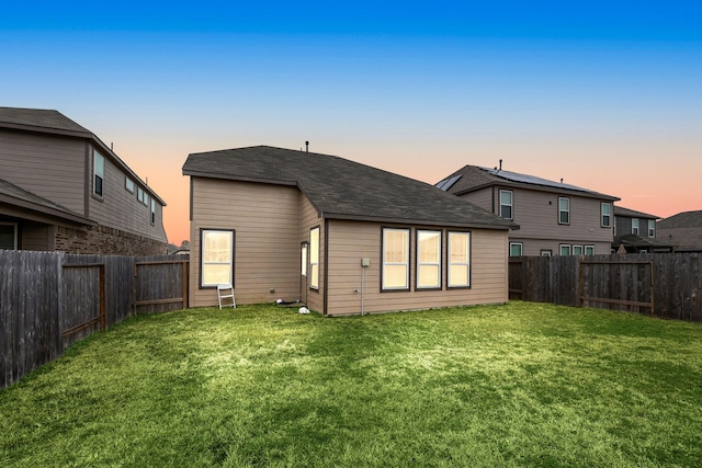 back house at dusk featuring a lawn