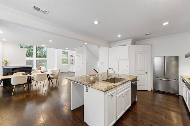 kitchen featuring sink, white cabinetry, stainless steel appliances, light stone counters, and an island with sink