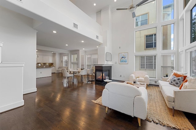 living room with a towering ceiling, dark hardwood / wood-style floors, ceiling fan, and a multi sided fireplace