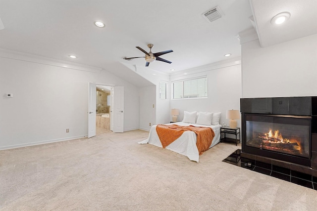 bedroom featuring a tile fireplace, ensuite bathroom, light colored carpet, ceiling fan, and crown molding