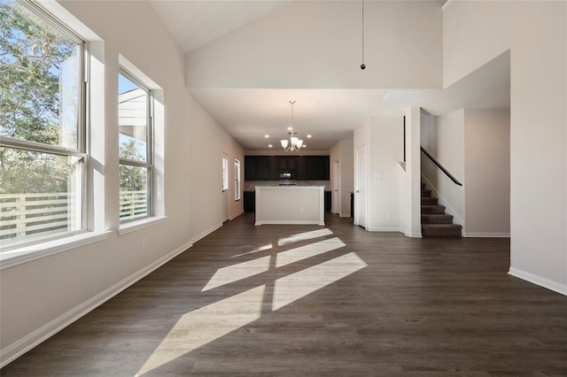 unfurnished living room with dark wood-type flooring, high vaulted ceiling, and a chandelier