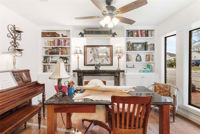 living area featuring built in shelves, light hardwood / wood-style flooring, and ceiling fan