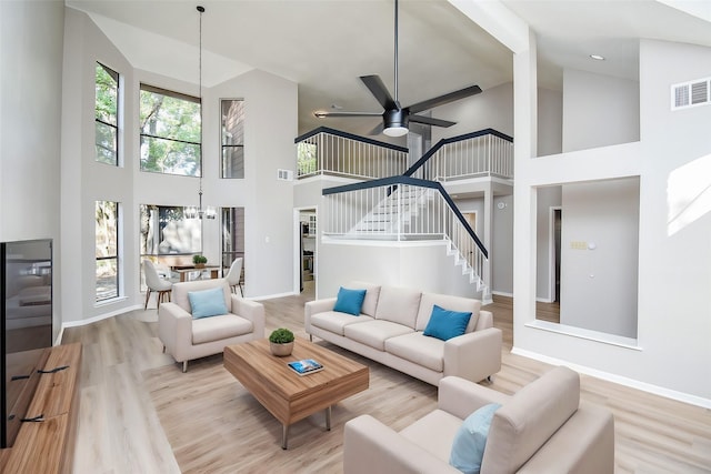 living room with high vaulted ceiling, ceiling fan with notable chandelier, and light wood-type flooring