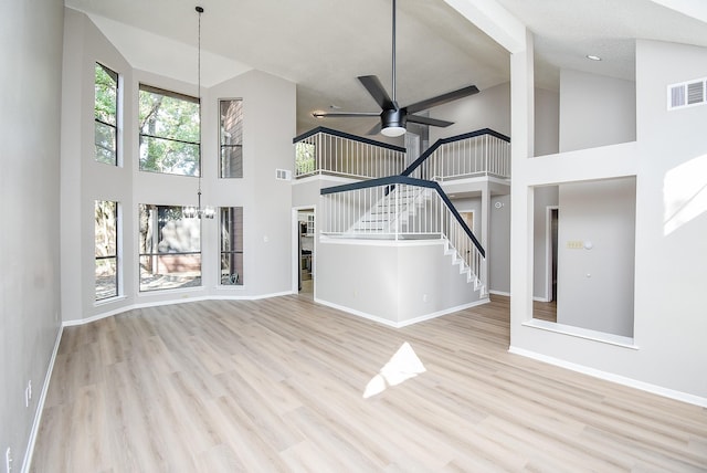 unfurnished living room with high vaulted ceiling, ceiling fan with notable chandelier, and light wood-type flooring