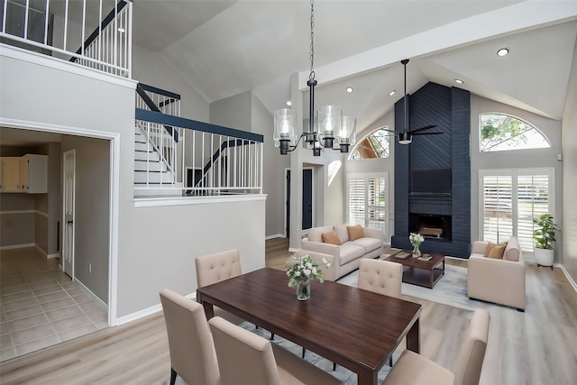 dining area featuring high vaulted ceiling, a notable chandelier, a fireplace, and light hardwood / wood-style flooring