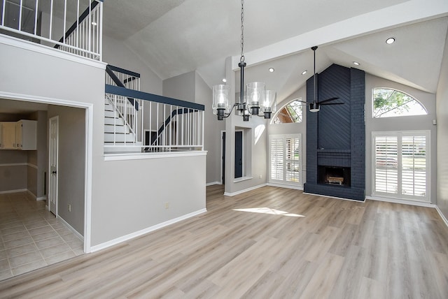 unfurnished living room with a brick fireplace, a notable chandelier, high vaulted ceiling, and light hardwood / wood-style floors