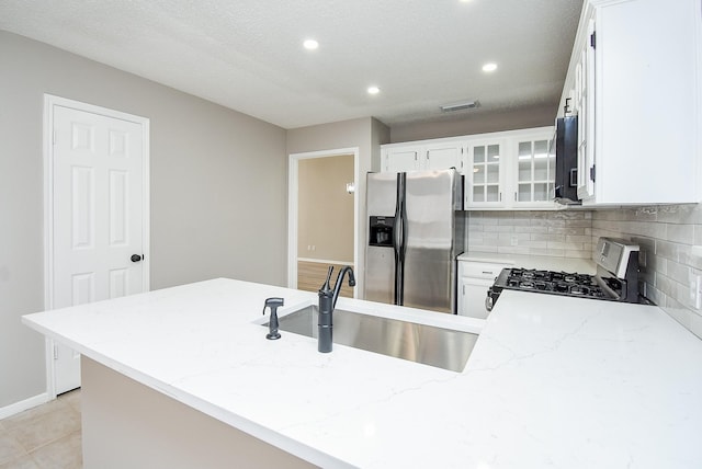 kitchen with appliances with stainless steel finishes, sink, white cabinets, kitchen peninsula, and light stone countertops