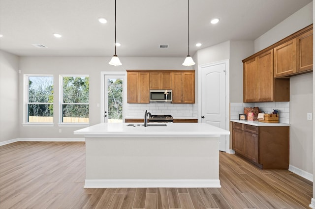 kitchen featuring sink, decorative light fixtures, light hardwood / wood-style flooring, a kitchen island with sink, and backsplash