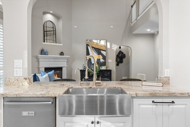 kitchen with light stone counters, dishwasher, sink, and white cabinets