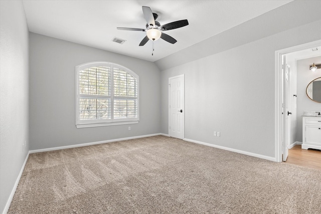 unfurnished bedroom featuring ceiling fan, light colored carpet, vaulted ceiling, and ensuite bath