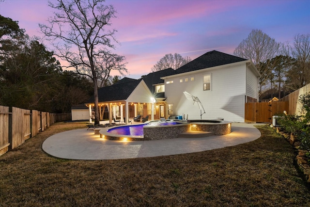 back house at dusk featuring a pool with hot tub and a patio area