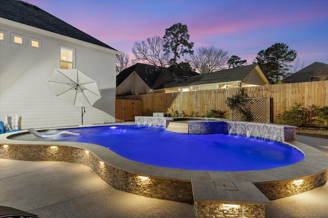 pool at dusk featuring pool water feature and an in ground hot tub