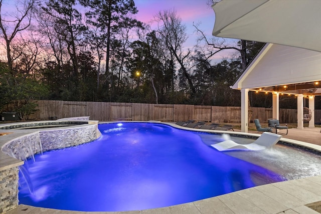 pool at dusk with an in ground hot tub, pool water feature, and a patio area