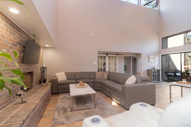 living room with a brick fireplace, light tile patterned floors, a barn door, and a high ceiling