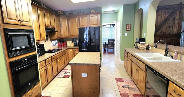 kitchen with light tile patterned flooring, sink, a center island with sink, and black appliances