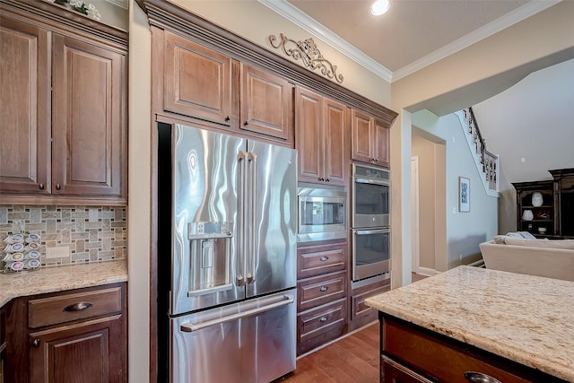 kitchen featuring crown molding, stainless steel appliances, tasteful backsplash, light stone countertops, and light wood-type flooring