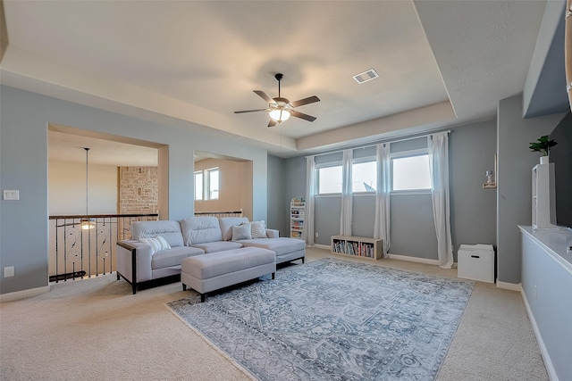 living room featuring a raised ceiling, light carpet, and ceiling fan