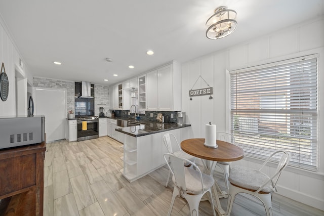 kitchen with stainless steel range oven, kitchen peninsula, white cabinets, decorative backsplash, and wall chimney range hood