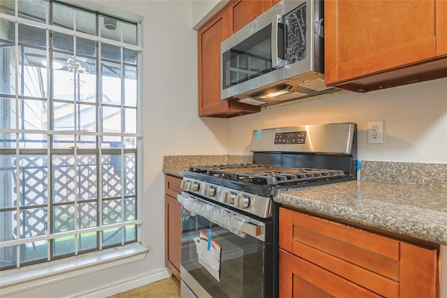 kitchen with stainless steel appliances, light tile patterned flooring, and light stone counters