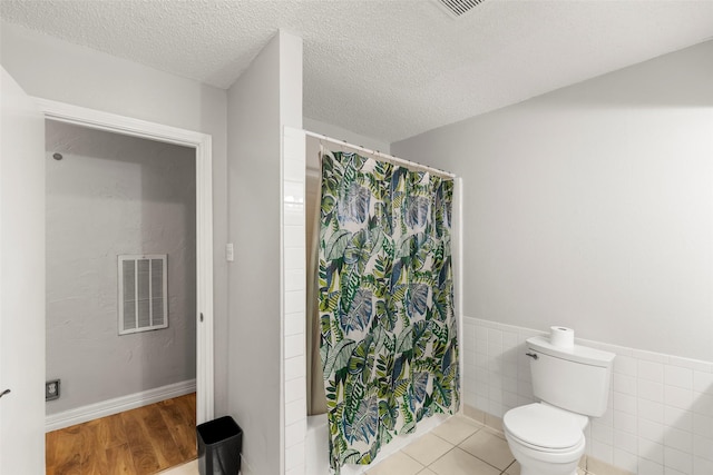 bathroom featuring shower / tub combo with curtain, toilet, a textured ceiling, tile walls, and hardwood / wood-style floors