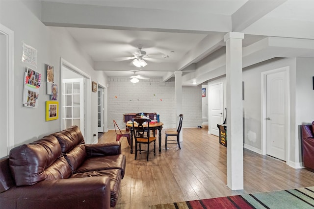 living room with beam ceiling, ceiling fan, brick wall, and light hardwood / wood-style floors