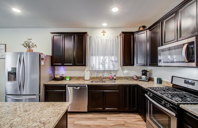 kitchen with sink, stainless steel appliances, light stone counters, dark brown cabinetry, and light wood-type flooring